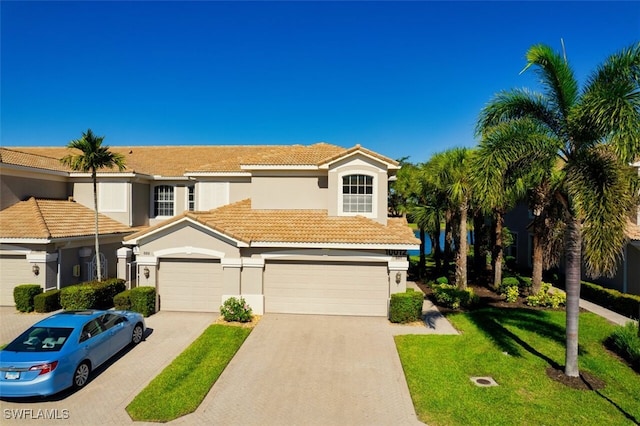 townhome / multi-family property featuring a tile roof, a front yard, stucco siding, driveway, and an attached garage