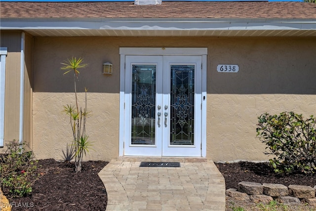 view of exterior entry featuring stucco siding, french doors, and a shingled roof