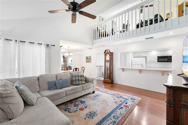 living area with visible vents, wood finished floors, a towering ceiling, and ceiling fan with notable chandelier