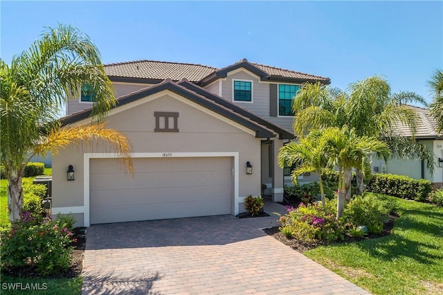 view of front of property featuring stucco siding, a tiled roof, decorative driveway, and a garage