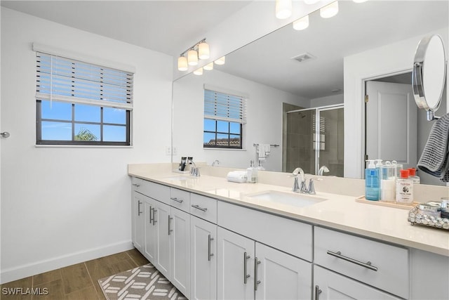 full bathroom featuring baseboards, visible vents, double vanity, a sink, and a shower stall