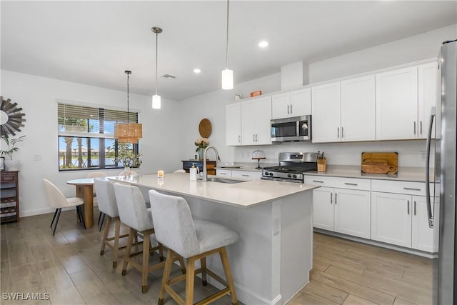 kitchen featuring a center island with sink, stainless steel appliances, light wood-type flooring, and a sink