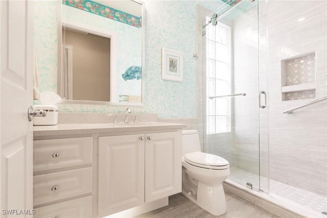 full bathroom featuring wallpapered walls, a shower stall, toilet, and vanity