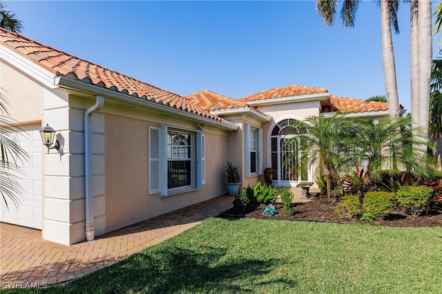 exterior space featuring a yard, stucco siding, a tiled roof, and a garage