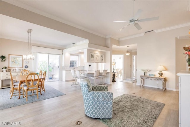 living area with ceiling fan with notable chandelier, baseboards, crown molding, and light wood-style floors