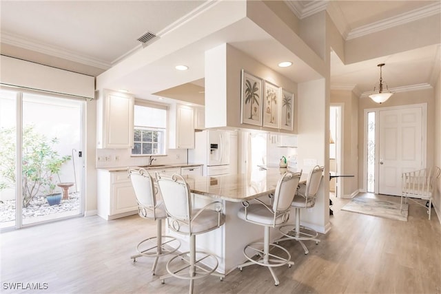 kitchen with a sink, a breakfast bar area, white fridge with ice dispenser, and ornamental molding