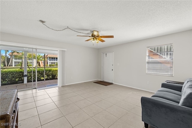 living area featuring light tile patterned flooring, a ceiling fan, baseboards, and a textured ceiling