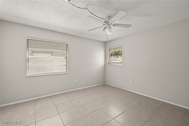 tiled spare room featuring a textured ceiling, baseboards, and a ceiling fan