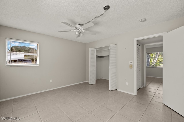 unfurnished bedroom featuring baseboards, light tile patterned floors, a closet, a textured ceiling, and a ceiling fan