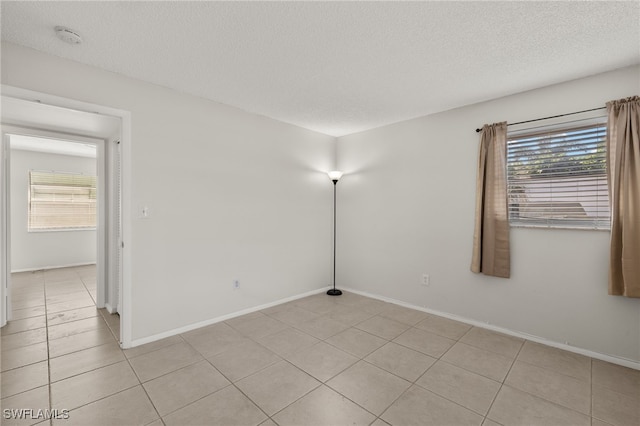 empty room with light tile patterned floors, baseboards, and a textured ceiling