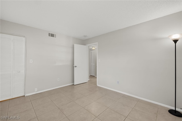 unfurnished bedroom with light tile patterned floors, visible vents, a textured ceiling, and baseboards