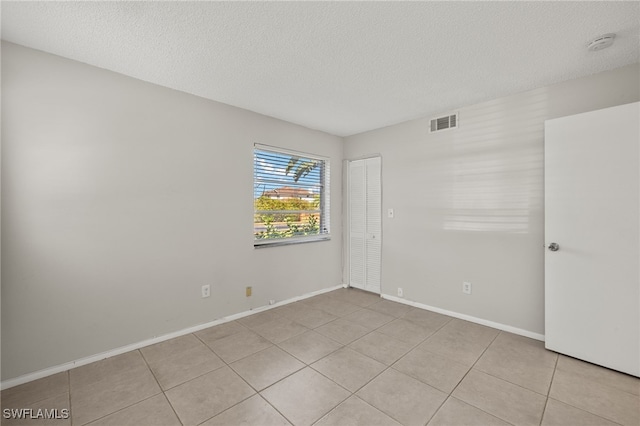 spare room with light tile patterned floors, baseboards, visible vents, and a textured ceiling