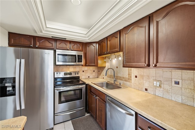 kitchen with backsplash, crown molding, appliances with stainless steel finishes, a raised ceiling, and a sink