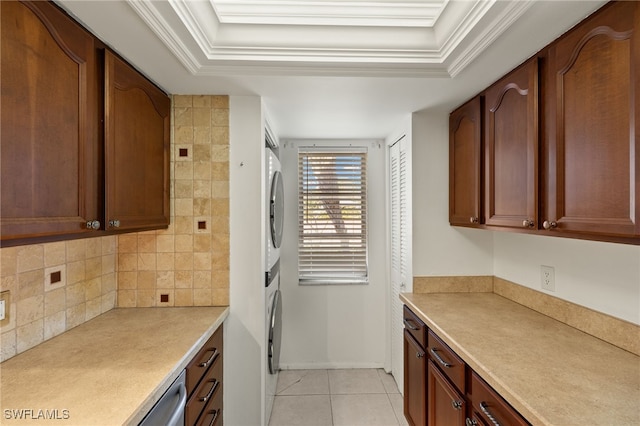 kitchen with stacked washer and clothes dryer, tasteful backsplash, light countertops, light tile patterned floors, and a raised ceiling