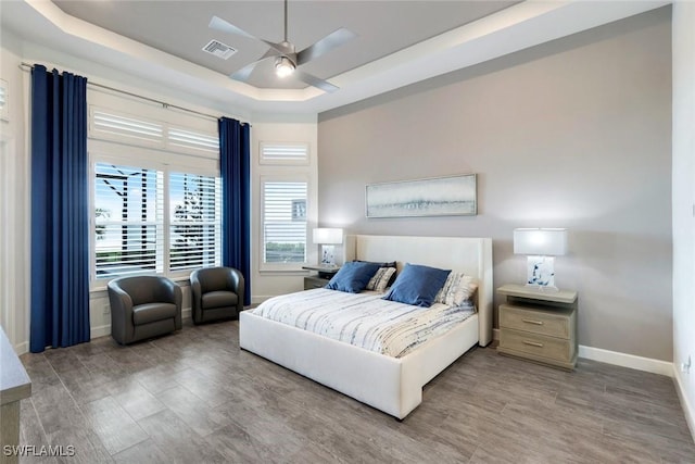 bedroom with wood finished floors, a tray ceiling, baseboards, and ceiling fan