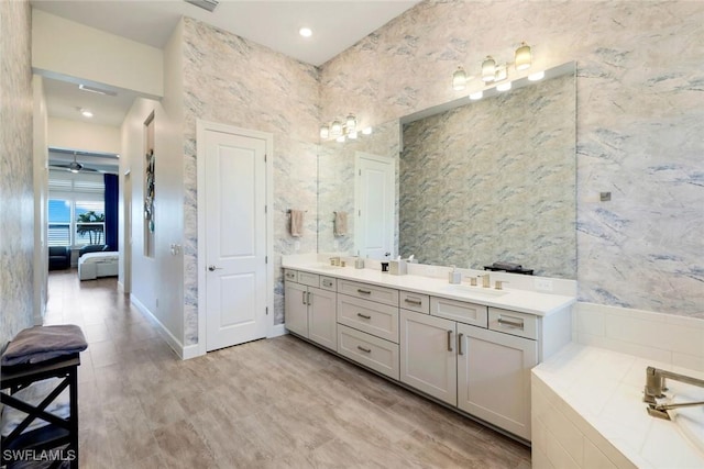 ensuite bathroom with connected bathroom, baseboards, a washtub, double vanity, and a sink