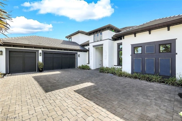 prairie-style home with stucco siding, a tile roof, decorative driveway, and a garage