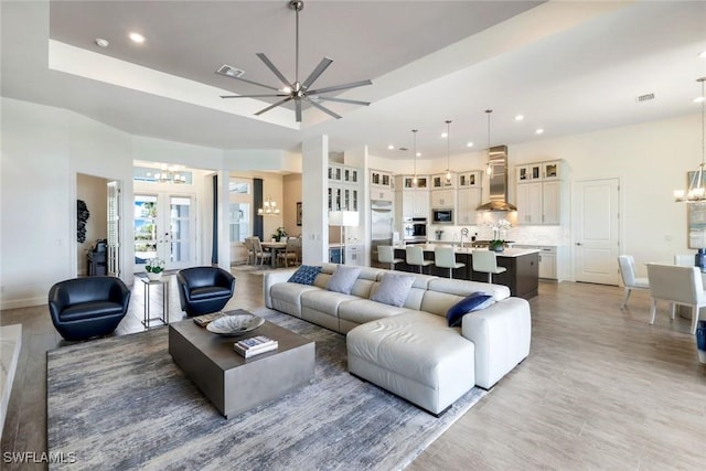 living area featuring a tray ceiling, visible vents, recessed lighting, and ceiling fan with notable chandelier