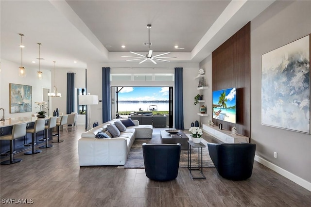 living area with a raised ceiling, a ceiling fan, wood finished floors, recessed lighting, and baseboards