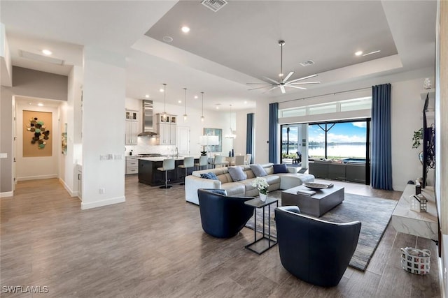 living room with a tray ceiling, wood finished floors, and visible vents