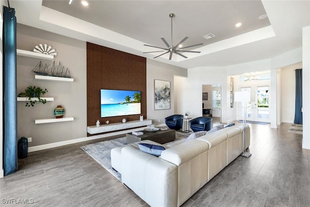 living area featuring visible vents, baseboards, a tray ceiling, ceiling fan with notable chandelier, and light wood-style floors