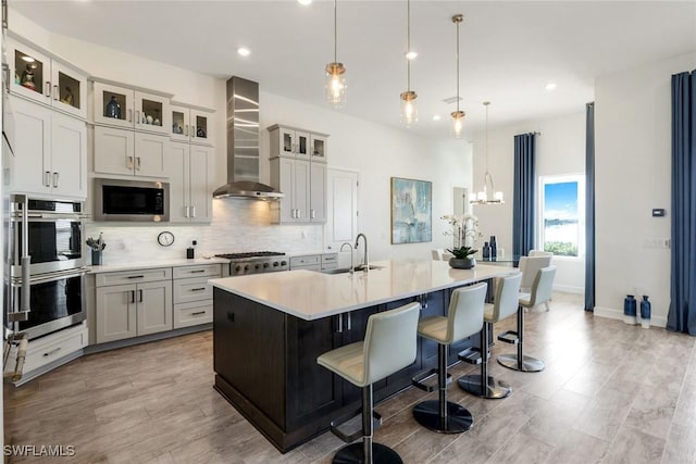 kitchen with a sink, wall chimney range hood, backsplash, appliances with stainless steel finishes, and light countertops