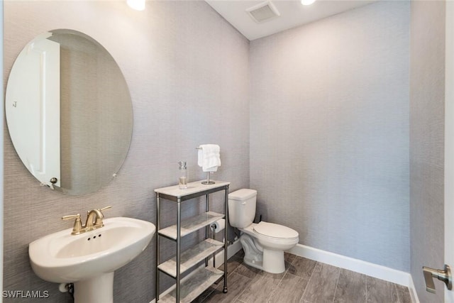 bathroom with visible vents, baseboards, wood tiled floor, toilet, and a sink