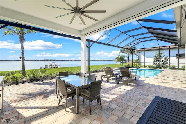 view of patio featuring glass enclosure, outdoor dining area, a ceiling fan, and a water view