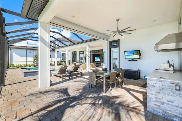 view of patio with area for grilling, glass enclosure, outdoor dining space, and a ceiling fan