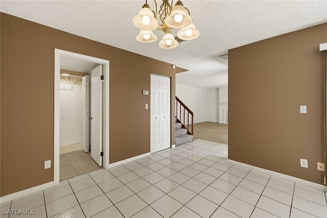 spare room featuring light tile patterned floors, a textured ceiling, an inviting chandelier, and stairs