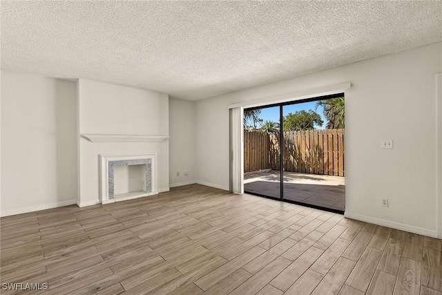 unfurnished living room featuring a fireplace, a textured ceiling, baseboards, and wood finished floors