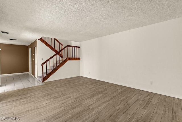 unfurnished room featuring stairway, a textured ceiling, visible vents, and wood finished floors