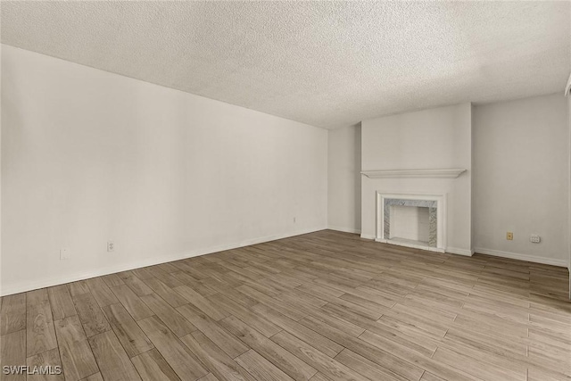 unfurnished living room featuring a high end fireplace, a textured ceiling, baseboards, and wood finished floors
