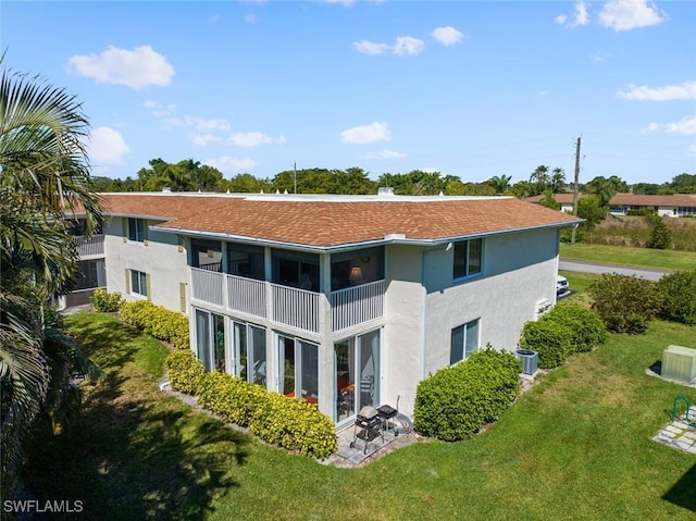 back of house featuring a shingled roof, central air condition unit, stucco siding, a lawn, and a balcony