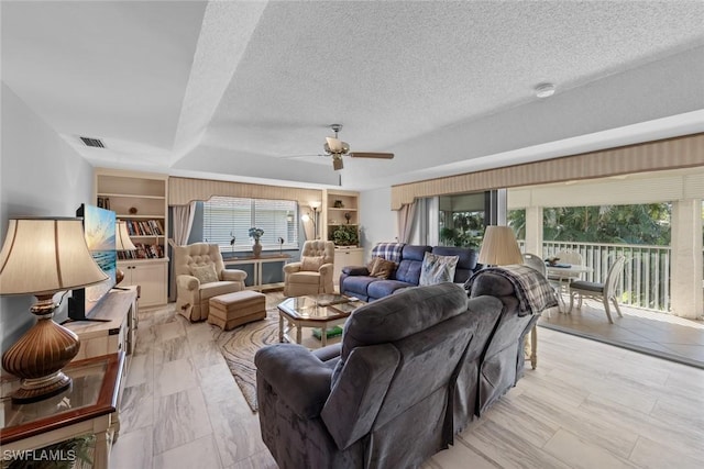 living room featuring visible vents, built in shelves, a textured ceiling, and ceiling fan