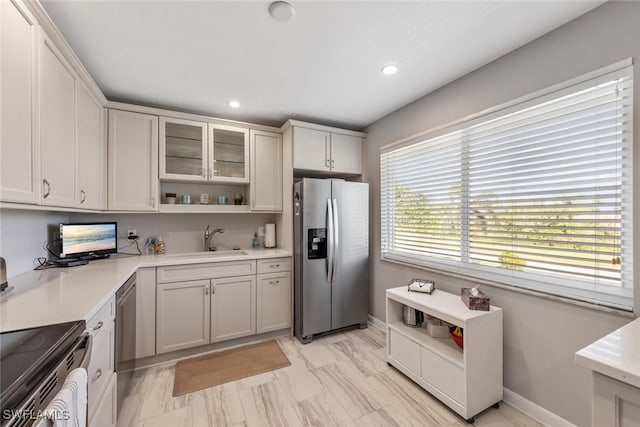 kitchen featuring open shelves, a sink, light countertops, glass insert cabinets, and appliances with stainless steel finishes