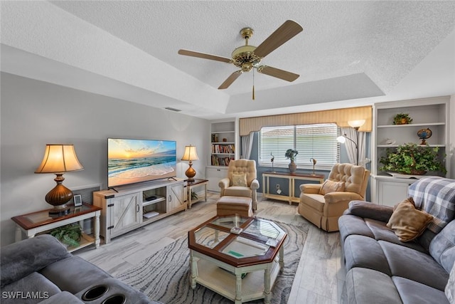 living room featuring built in shelves, a textured ceiling, a raised ceiling, and ceiling fan