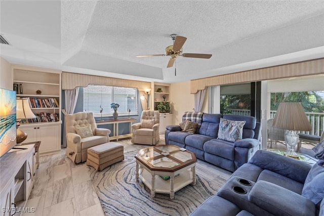 living area with built in features, a ceiling fan, a textured ceiling, a raised ceiling, and marble finish floor