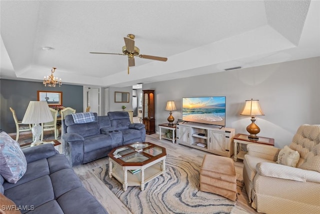 living room featuring a tray ceiling, ceiling fan with notable chandelier, and visible vents