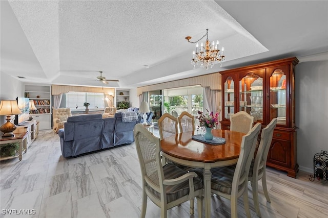 dining space featuring ceiling fan with notable chandelier, built in shelves, a textured ceiling, and a tray ceiling