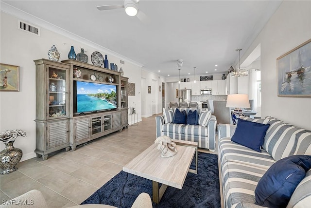 living area featuring visible vents, baseboards, ornamental molding, light tile patterned floors, and ceiling fan with notable chandelier