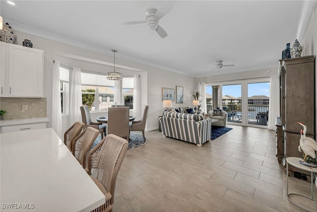 living area with crown molding, ceiling fan with notable chandelier, and baseboards