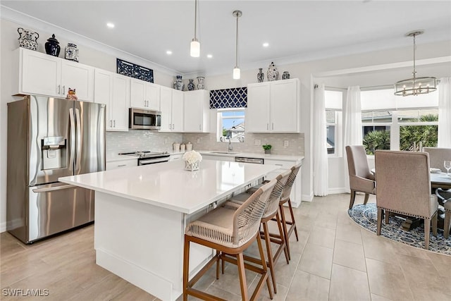 kitchen featuring backsplash, a center island, light countertops, ornamental molding, and stainless steel appliances