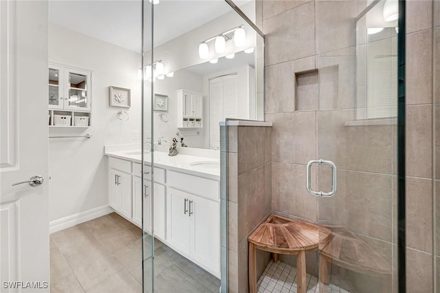 bathroom with tile patterned floors, a sink, a shower stall, double vanity, and baseboards