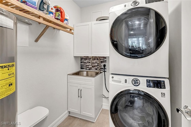 washroom featuring a sink, baseboards, cabinet space, and stacked washer and clothes dryer