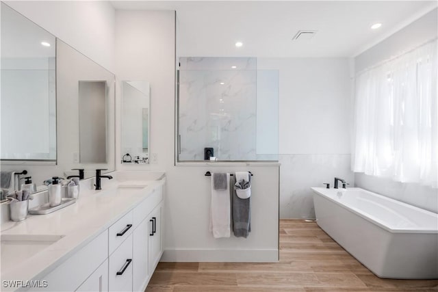 full bath featuring a freestanding tub, a sink, wood finished floors, recessed lighting, and double vanity