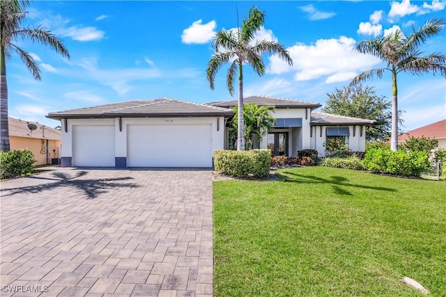 prairie-style home featuring a front lawn, a tiled roof, stucco siding, decorative driveway, and a garage