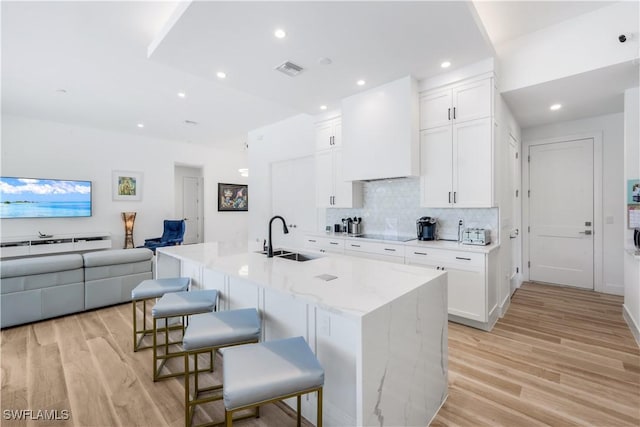 kitchen with a sink, light wood-type flooring, white cabinetry, and custom range hood