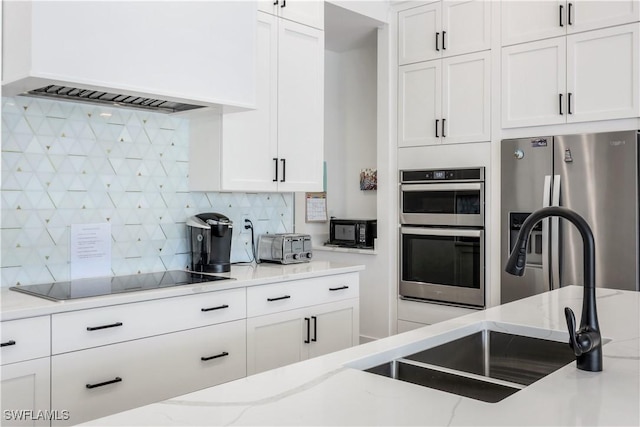 kitchen featuring black appliances, custom range hood, a sink, white cabinets, and decorative backsplash