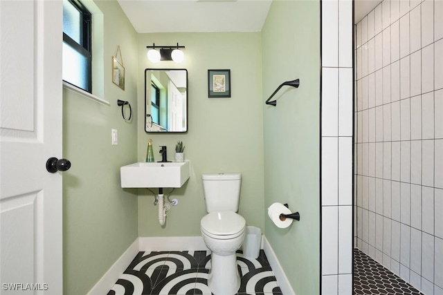 full bath with tile patterned flooring, baseboards, toilet, a tile shower, and a sink